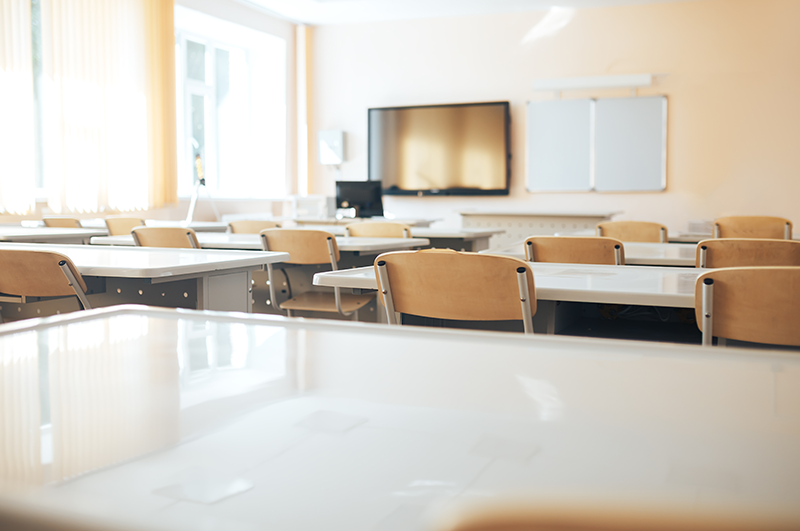 bright, empty classroom with white tables, chairs and a large screen